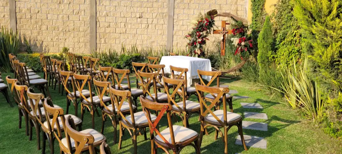 Ceremonia religiosa en el jardín de Bonanza: cruz con arco de flores rojas y mesa de altar bajo la luz dorada de la tarde