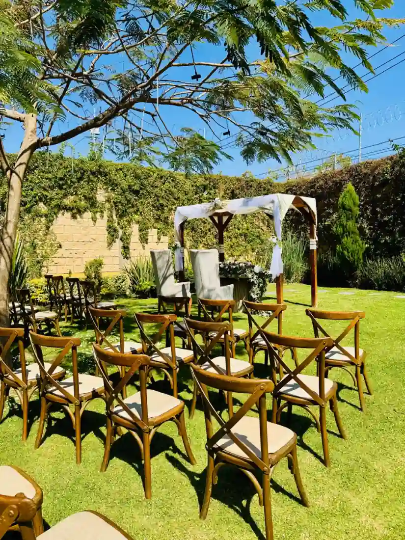 Pérgola de madera con telas blancas y sillas de madera bajo el cielo azul, en el jardín del salón en Tonalá