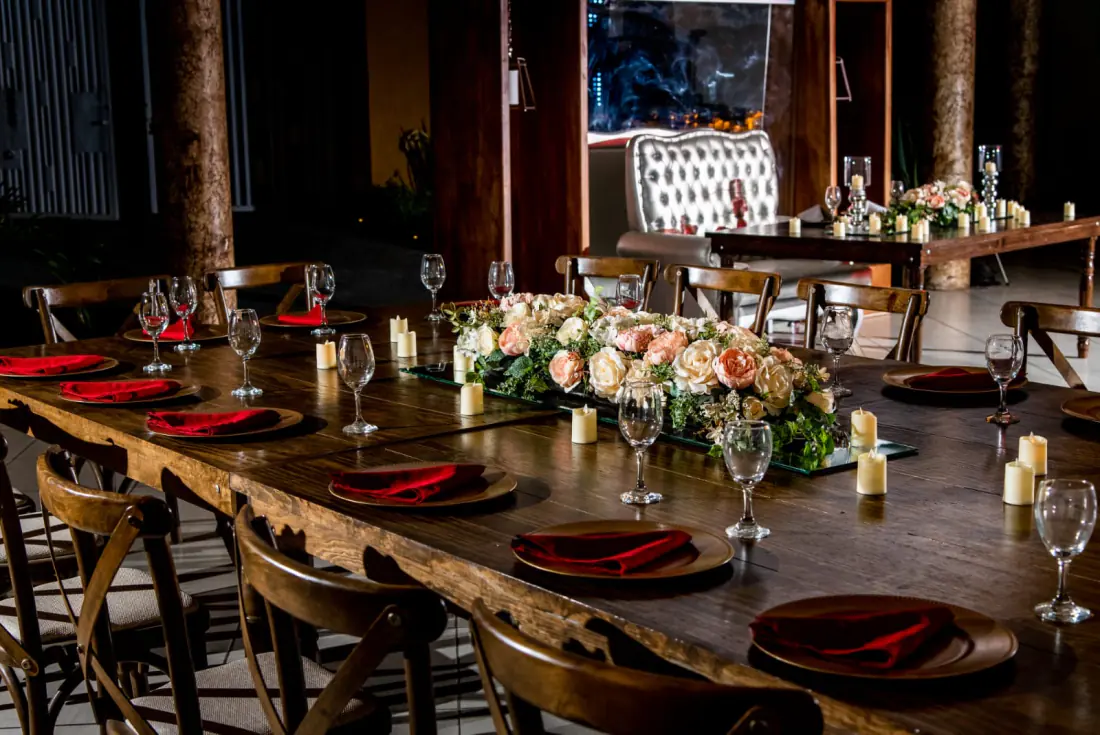 Salón para XV años de noche: mesas de madera con servilletas rojas y el sillón de la festejada al fondo