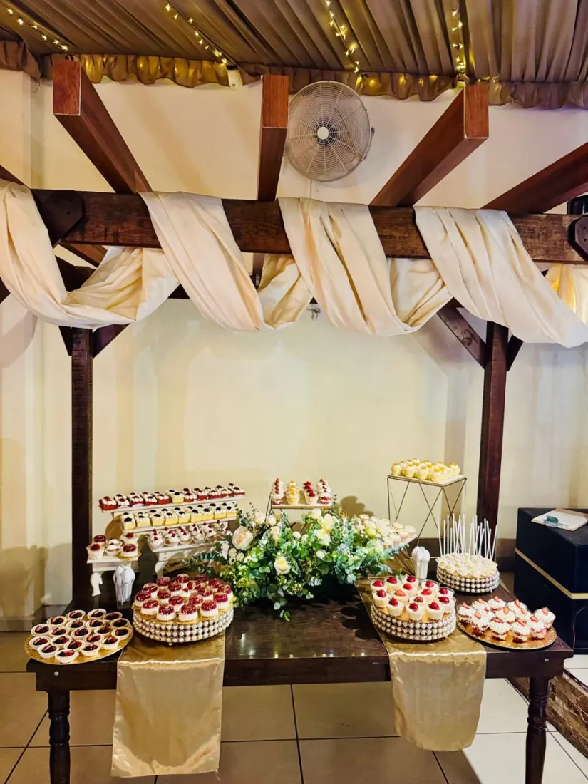 Mesa de postres bajo el drapeado de la terraza, con bocadillos, flores y luces colgando de las vigas