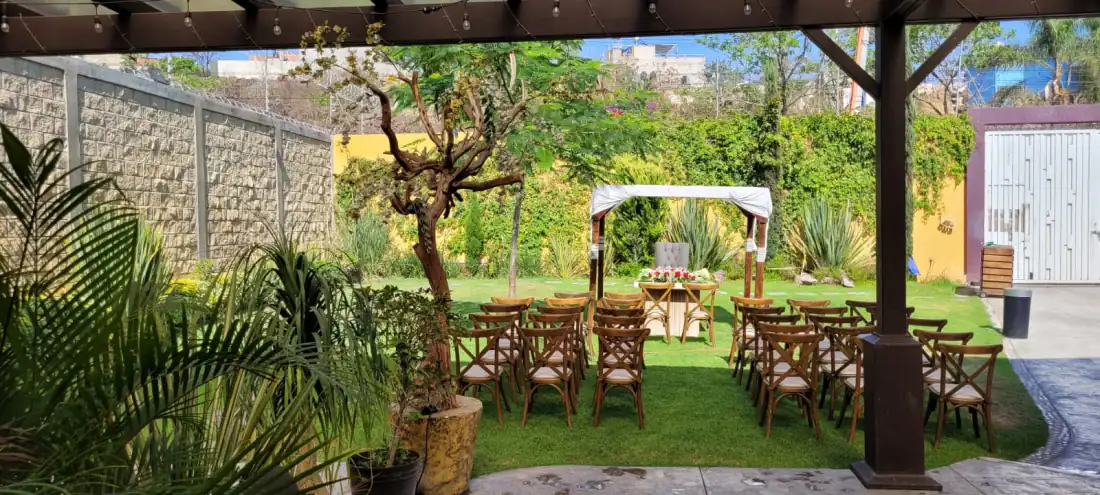 Pérgola de madera de la terraza sobre el pasto del jardín, con sillas crossback y muro de piedra