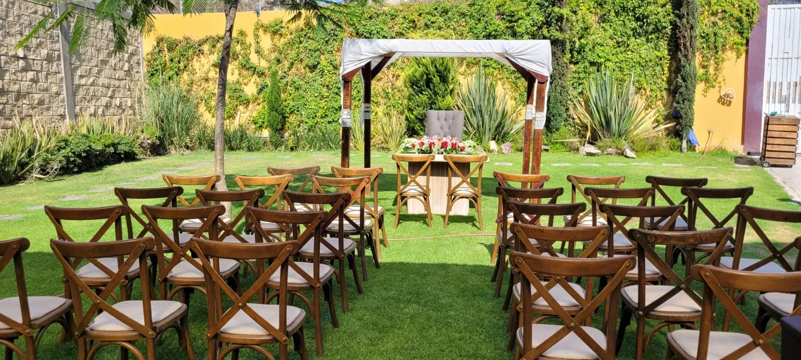 Jardín de Bonanza con pérgola blanca, muros de enredadera y sillas de madera listas para la ceremonia